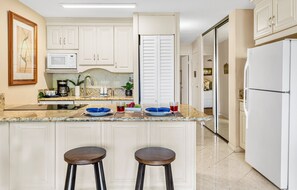 A kitchen with white cabinets, a microwave, a refrigerator, and two stools. - Tropical Retreat, steps from Charlie Young Beach (Kihei)