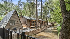 Una cabaña de troncos con un porche y un pequeño puente sobre un arroyo.