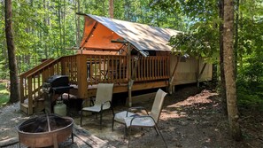 Una cabaña con terraza, una parrilla, sillas y un hogar para la fogata.