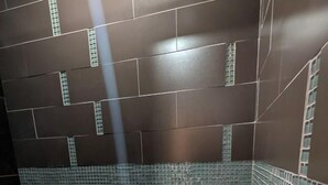 A bathroom with dark tiled walls, a small shelf with a green bottle, and a textured floor. - Secluded Off-Grid Glamping Tent with Private Bathhouse Near The Caverns & Waterfalls – Coalmont, Tennessee (Coalmont)