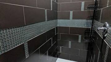 A modern bathroom with dark tiles, a shower area, and a tiled floor.