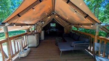 Een tentaccomodatie met een houten terras, een bank, een kleine tafel en een televisie.
