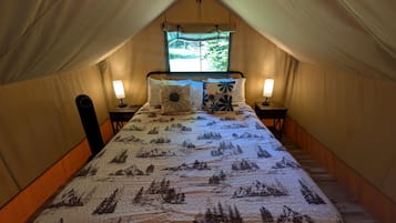 A tented room with a bed, two bedside lamps, and a window with a view of greenery.