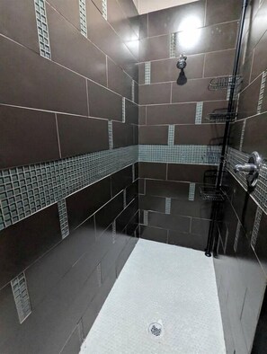 A modern bathroom with dark tiles, a shower area, and a tiled floor.