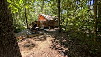 Uma cabana numa floresta com lareira e área de estar ao ar livre.