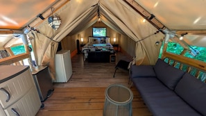Un alojamiento con carpa que incluye kitchenette, sofá y cama con vistas al exterior.