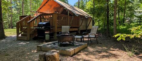 A rustic cabin with a wooden deck, a fire pit, and a grill area.
