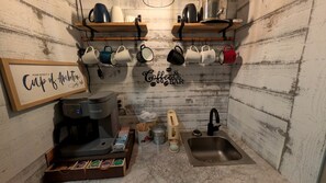 A small kitchenette with a coffee machine, mugs, a sink, and a framed sign.
