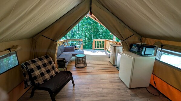 A tent with a wooden deck, a sofa, a small table, a microwave, and a TV.