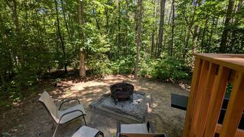 A forested outdoor area with a fire pit and seating.