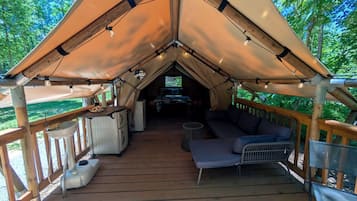 A tented accommodation with a wooden deck, a sofa, a small table, and a television.