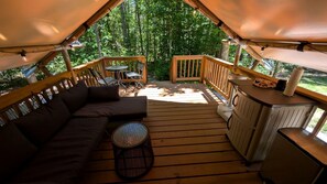Eine Zelthütte mit Holzterrasse, einer Couch, einem runden Tisch und einer Küchenzeile.