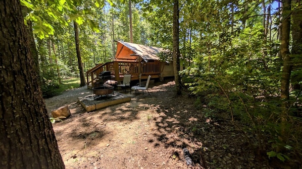 Una cabaña en un bosque con una fogata y asientos al aire libre.