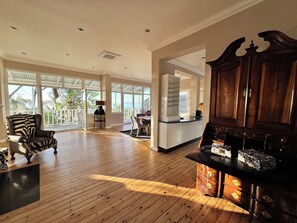 Ein geräumiges Wohnzimmer mit Holzboden, einem zebra-gestreiften Sessel, einem Holzschrank und Blick durch große Fenster.
