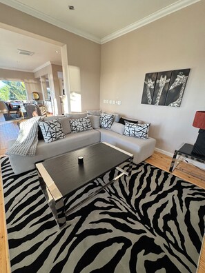A modern living room with a sectional sofa, a zebra-patterned rug, and a wall-mounted artwork of giraffes. - Luxury one bedroom apartment in Green Point with AC, a pool and a view. (Cape Town)
