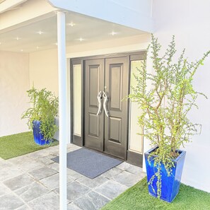 A building entrance with a dark wooden door, two potted plants, a doormat, and a tiled patio. - Luxury one bedroom apartment in Green Point with AC, a pool and a view. (Cape Town)