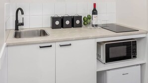 Eine Küche mit weißen Schränken, einer Edelstahl-Spüle, einem schwarzen Wasserhahn, einer Mikrowelle und einer Weinflasche.