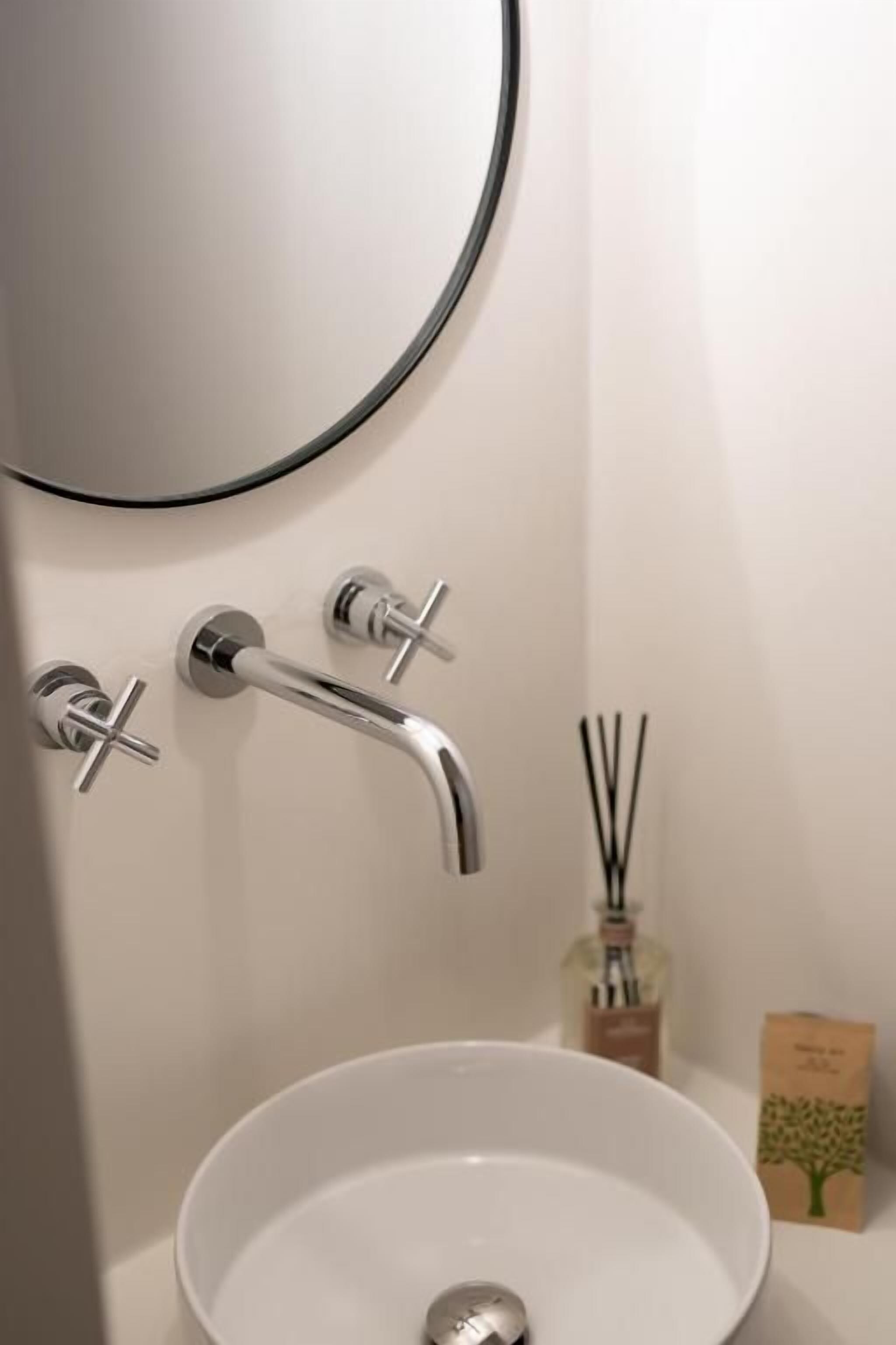 A bathroom with a round mirror, a white sink, and two faucets.