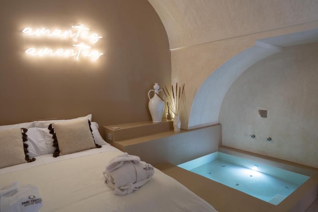 Habitación de hotel con cama, mesita de noche, luz empotrada en la pared y bañera integrada.