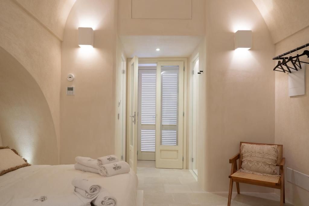 A hotel room with a bed, a chair, a door with blinds, and wall-mounted lights.