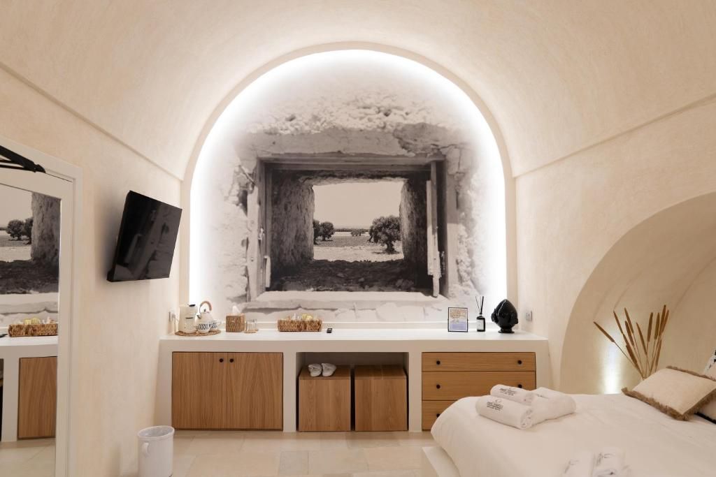 Une chambre à coucher avec une grande fenêtre en arc de cercle, un lit recouvert de draps blancs, une table de chevet et un miroir.