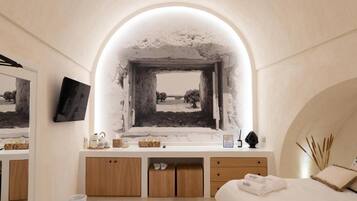 Une chambre à coucher avec une grande fenêtre en arc de cercle, un lit recouvert de draps blancs, une table de chevet et un miroir.