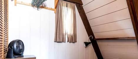 Ein Schlafzimmer mit schrägen Wänden, einem Bett mit gestreifter Decke, einer hölzernen Kommode und einem Deckenventilator.
