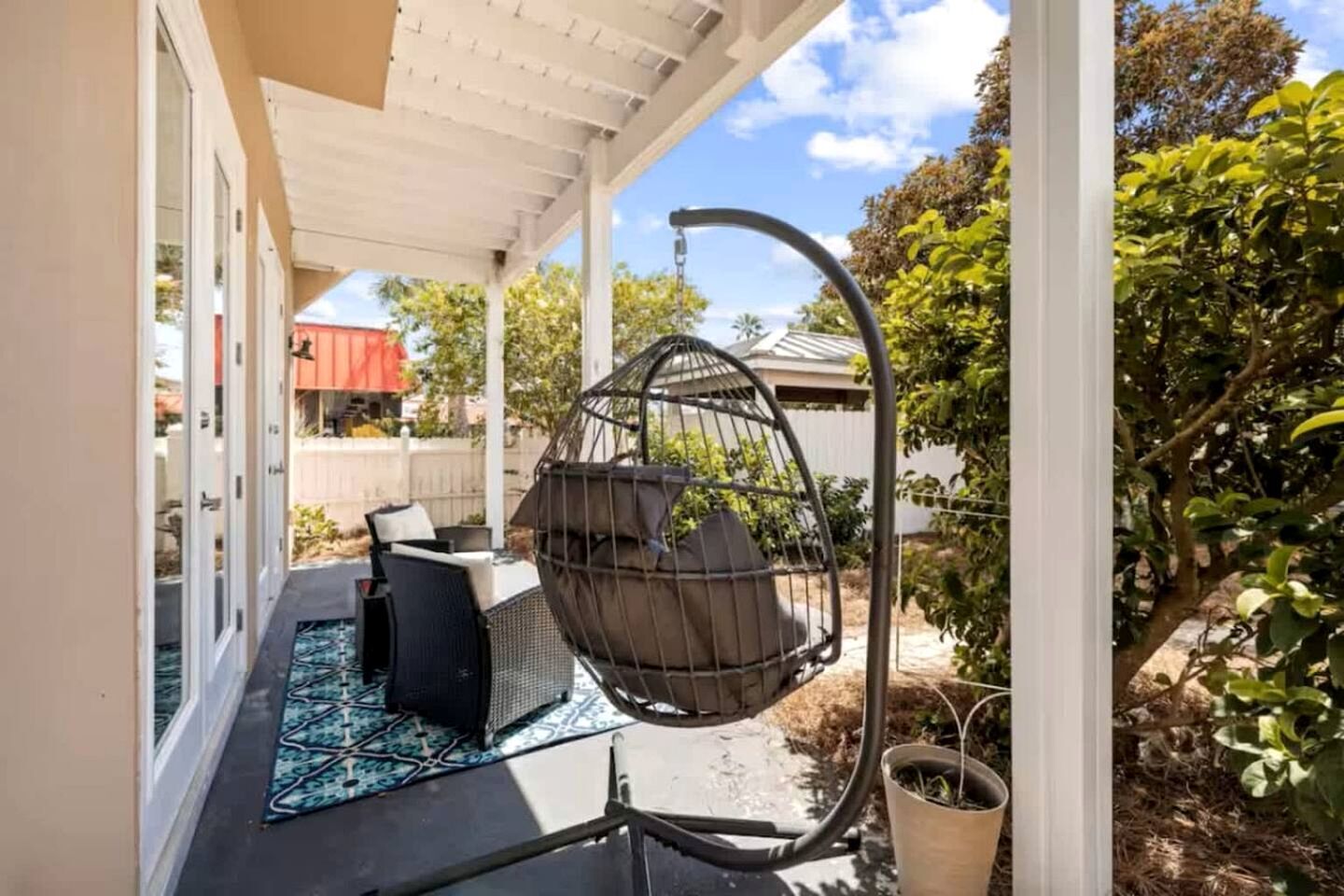 A covered patio with a hanging chair, outdoor furniture, and a potted plant.