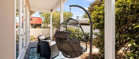 A covered patio with a hanging chair, outdoor furniture, and a potted plant.