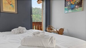 Quarto de hotel com cama, toalhas, uma cadeira de madeira e um quadro na parede.