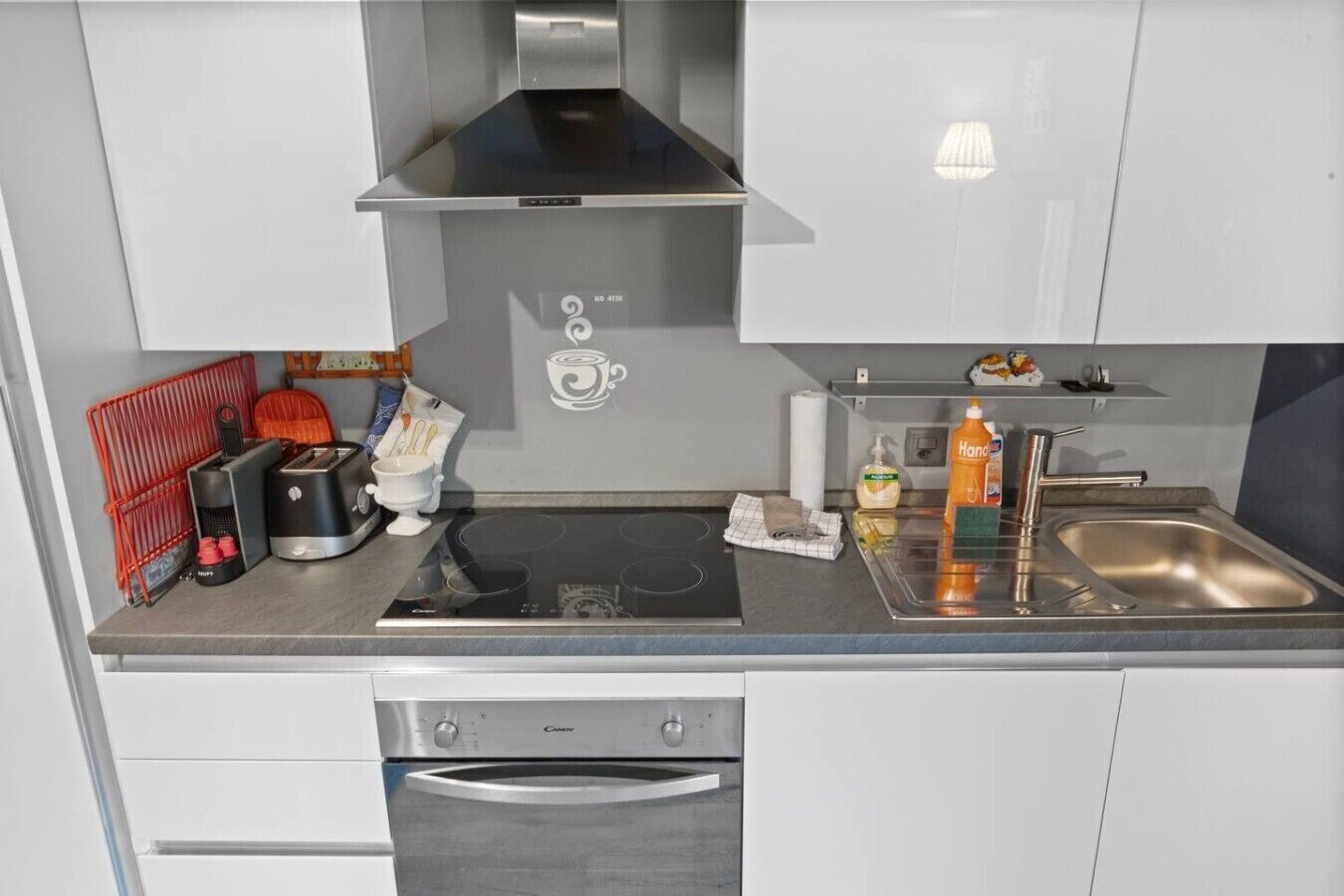 A modern kitchen with a built-in oven, a stainless steel sink, and a coffee machine.