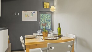 Uma área de refeições com uma mesa posta para dois, uma garrafa de vinho e uma janela com vista para uma floresta.