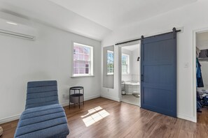 Een kamer met een blauwe stoel, een schuifdeur en uitzicht op een badkamer.
