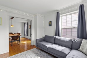 Een woonkamer met een grijze bank, een houten eettafel, stoelen en een kamerkleed met een patroon.