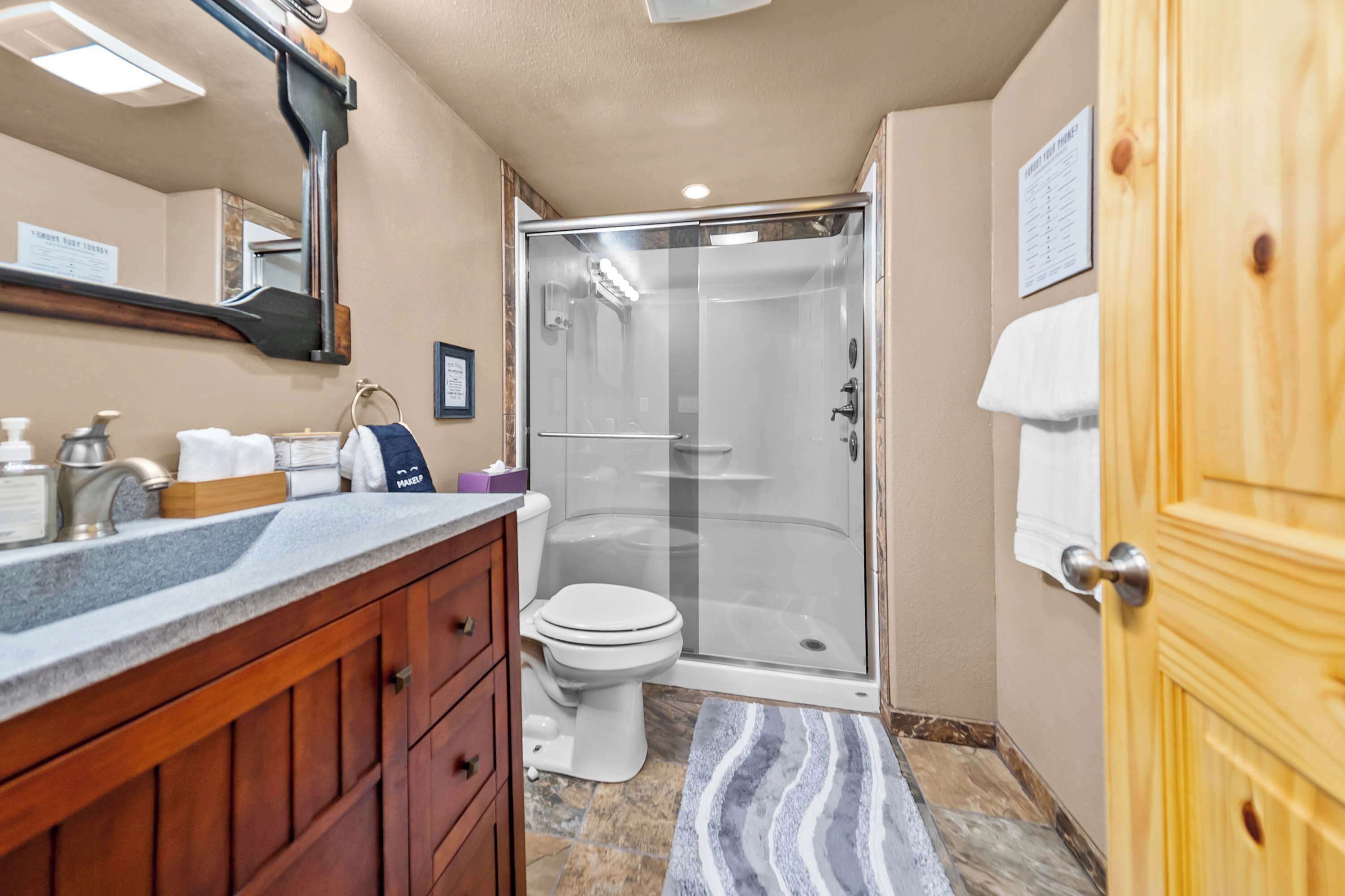 A bathroom with a shower, toilet, vanity, and a wooden door.