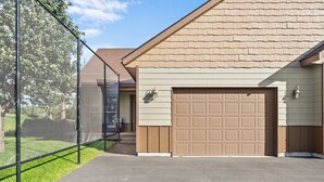Un garaje residencial con puerta marrón, patio cercado y una casa con techo inclinado.