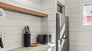 Cozinha com geladeira de aço inoxidável, torradeira e tábua de corte de madeira no balcão.