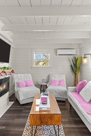 A modern living room with white walls, two sofas, a coffee table, a fireplace, and a large window. - Cupids Cottage Hot Tub, BBQ + Deck,  Parking (Cupids)