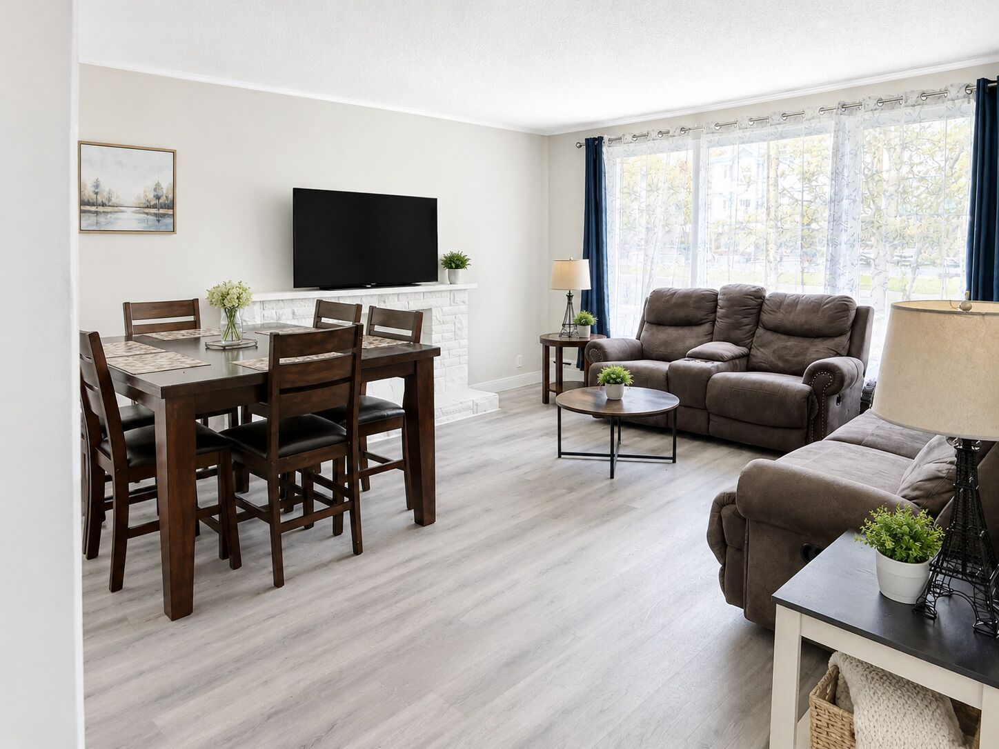 A living room with a dining area, a sofa, a TV, and a window with curtains.