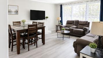 A living room with a dining area, a sofa, a TV, and a window with curtains.