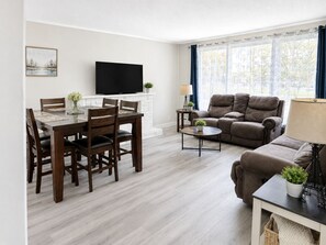 A living room with a dining area, a sofa, a TV, and a window with curtains. - Elizabeth Ave 3BR Stay Parking  Pet Friendly (St. John's)