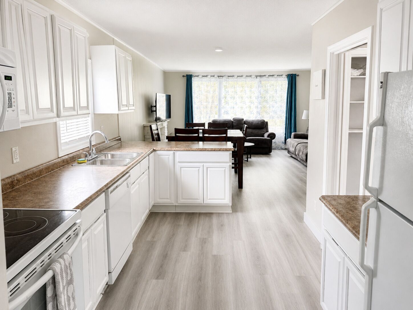 A modern kitchen with white cabinetry, a built-in oven, and a dining area with a table and chairs.