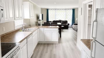 A modern kitchen with white cabinetry, a built-in oven, and a dining area with a table and chairs.