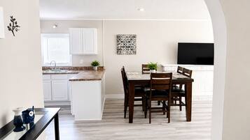 A modern kitchen with white cabinets, a granite countertop, and a dining area with wooden chairs and a table.