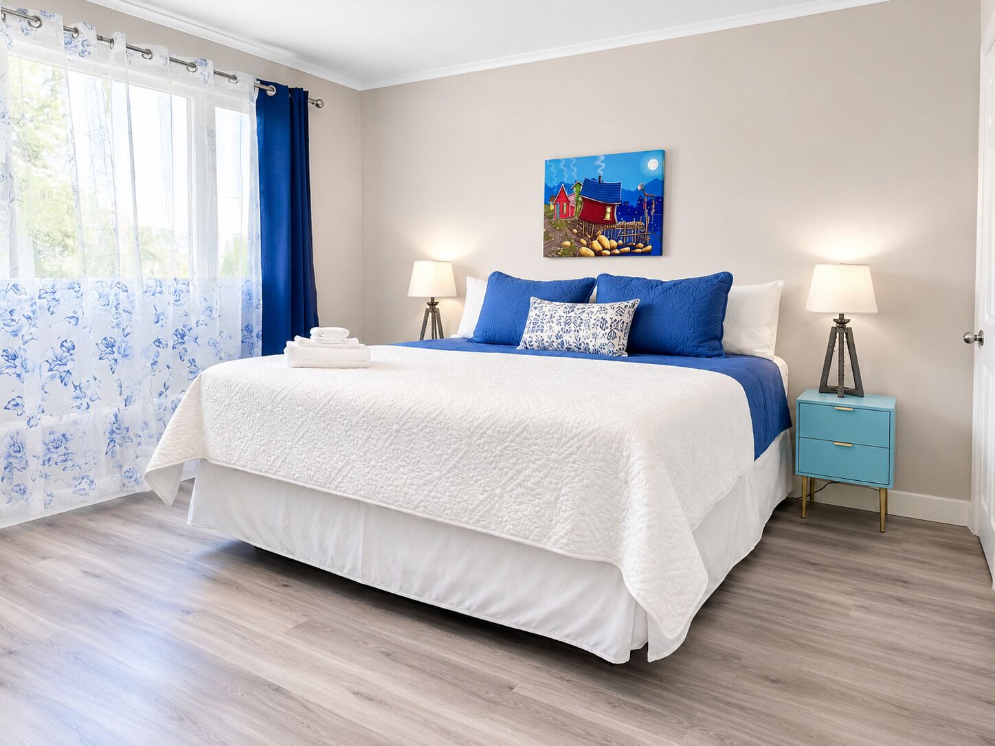 A bedroom with a bed, two bedside tables, a painting, and a window with curtains.