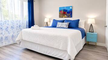 A bedroom with a bed, two bedside tables, a painting, and a window with curtains.