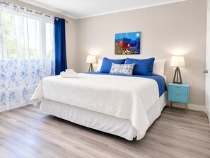 A bedroom with a bed, two bedside tables, a painting, and a window with curtains. - Elizabeth Ave 3BR Stay Parking  Pet Friendly (St. John's)