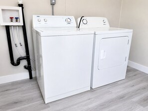 Een wasserette met twee witte voorladers, een witte plank met wat spullen en zwarte leidingen.