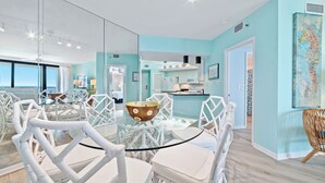 A modern kitchen with a glass island, white chairs, and a view of the ocean. - Beachfront Corner Views, Indoor & Outdoor Pools, Walk to Dining | BEACHBALL PROPERTIES (Orange Beach)