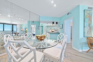 A modern kitchen with a glass island, white chairs, and a view of the ocean. - Beachfront Corner Views, Indoor & Outdoor Pools, Walk to Dining | BEACHBALL PROPERTIES (Orange Beach)